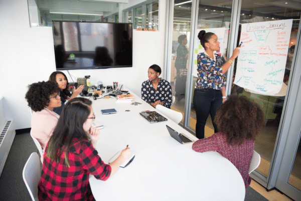 A photo of two employees gossiping behind another employee’s back, illustrating the concept of workplace harassment. 