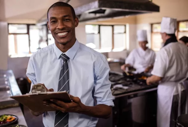 person checking list in front of three chefs in a kitchen