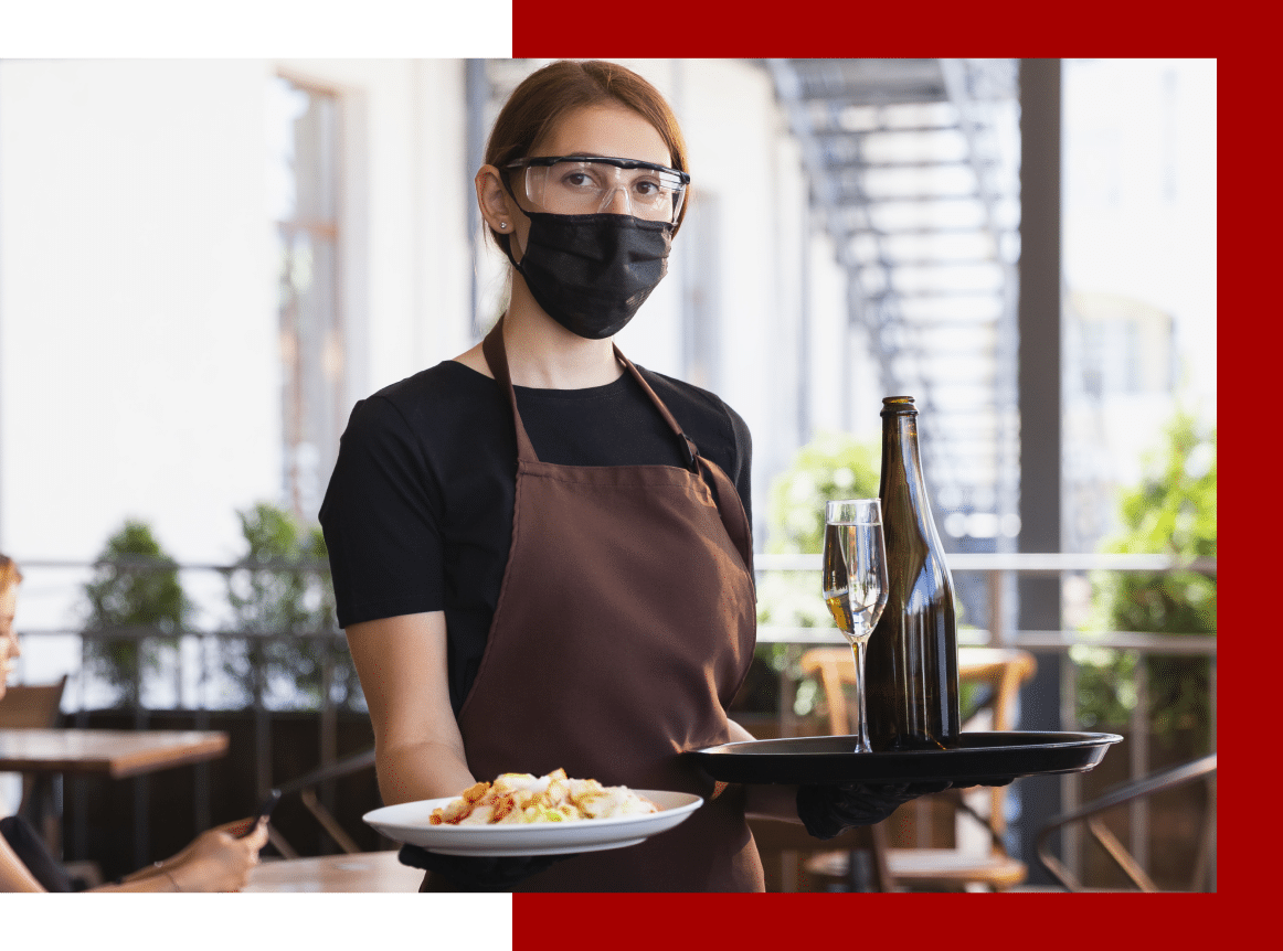 Food server carrying food while wearing a face mask and protective glasses.