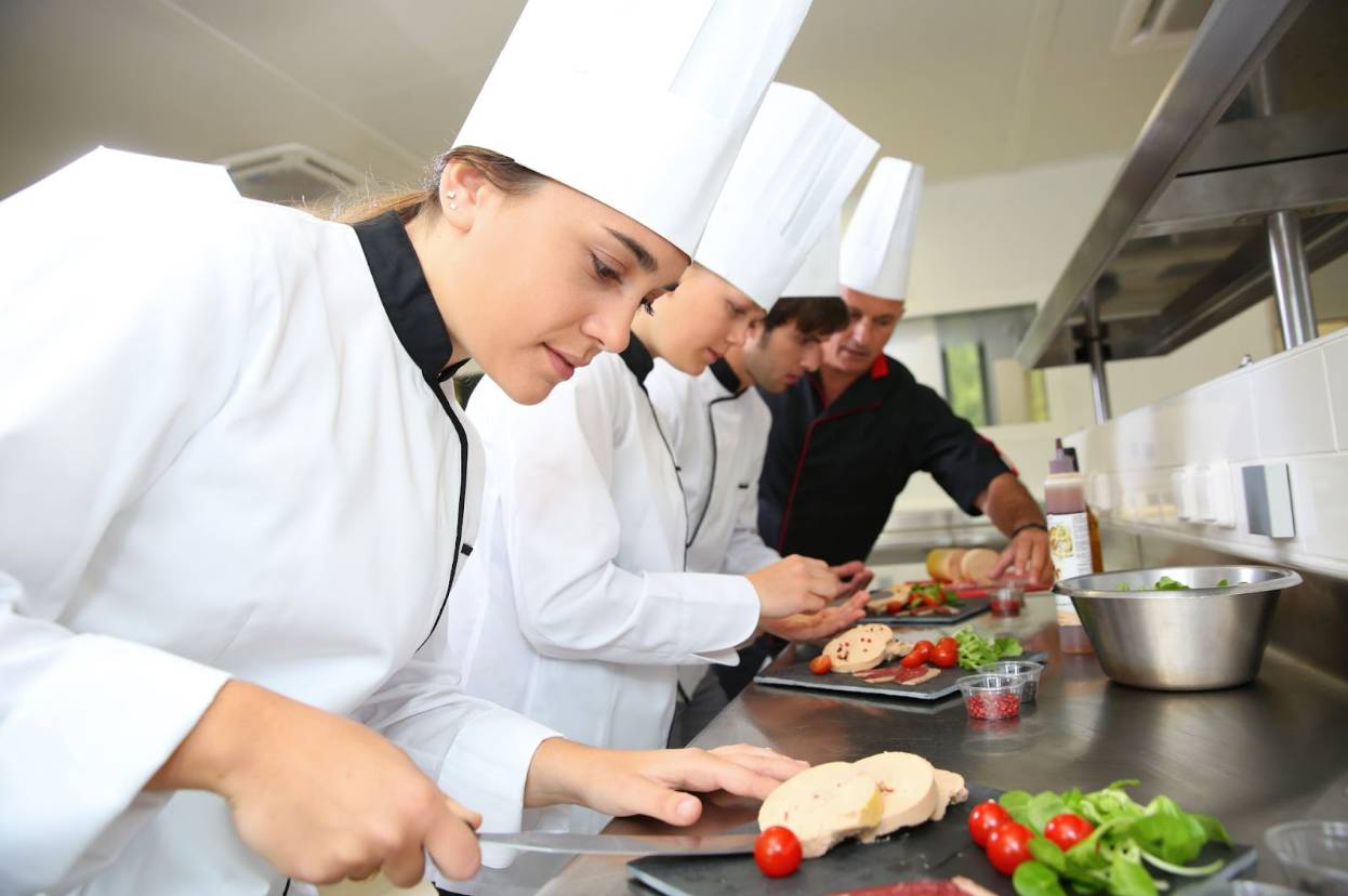 Chefs in white uniforms preparing food on a commercial kitchen line during food handler training